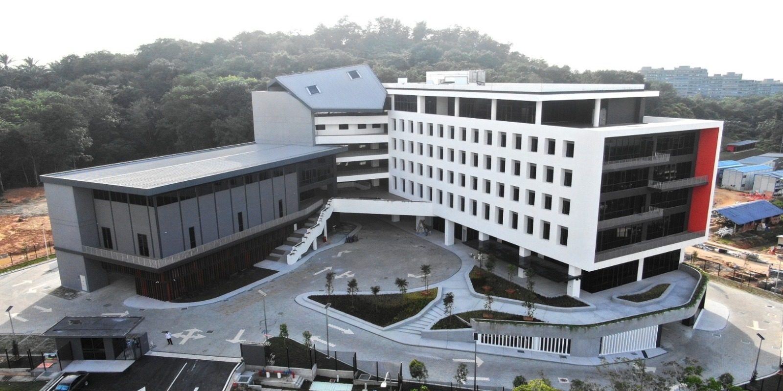 Aerial view of a modern multi-storey building complex with a landscaped forecourt, set against a forested hill.